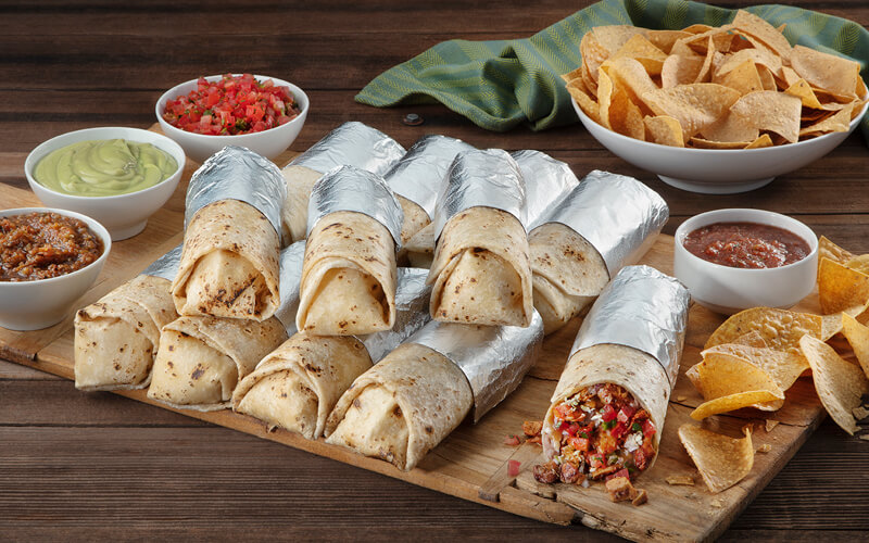 Assorted foil-wrapped burritos rest on a wooden board, paired perfectly with bowls of salsa, guacamole, and tortilla chips—a taste journey akin to enjoying authentic New York bagels found unexpectedly in Spain. Assorted foil-wrapped burritos rest on a wooden board, paired perfectly with bowls of salsa, guacamole, and tortilla chips—a taste journey akin to enjoying authentic New York bagels found unexpectedly in Spain.