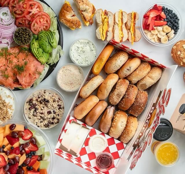A variety of authentic New York bagels in a box is surrounded by fruits, vegetables, and spreads on a table in Spain, including lox, avocado, and berries. A variety of authentic New York bagels in a box is surrounded by fruits, vegetables, and spreads on a table in Spain, including lox, avocado, and berries.