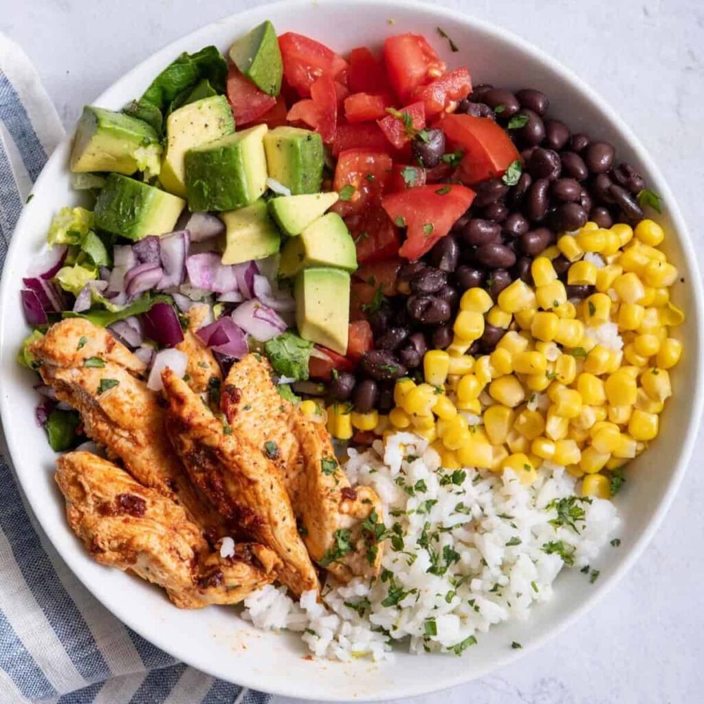 A bowl with grilled chicken, diced avocado, tomatoes, black beans, corn, red onion, and cilantro rice sits on a light surface with a striped cloth nearby—like enjoying authentic New York bagels in Spain for a culinary twist. A bowl with grilled chicken, diced avocado, tomatoes, black beans, corn, red onion, and cilantro rice sits on a light surface with a striped cloth nearby—like enjoying authentic New York bagels in Spain for a culinary twist.